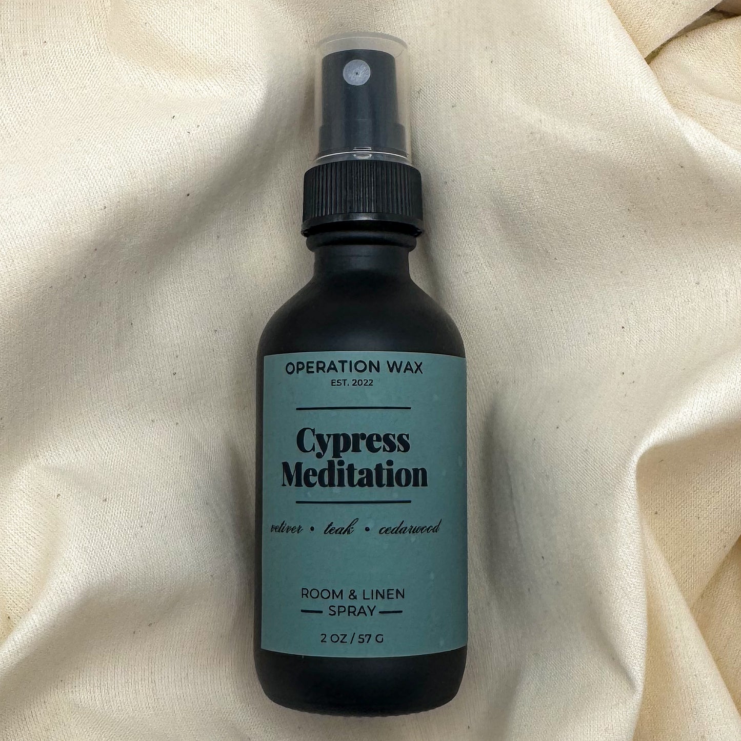 Room spray bottle labeled 'Cypress Meditation' on a textured beige fabric background