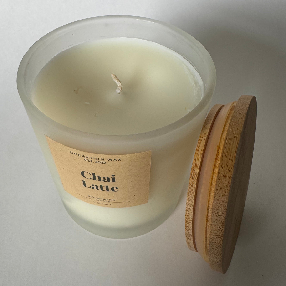 A frosted glass candle jar filled with creamy off-white wax, featuring a tan paper label that reads 'Chai Latte' and 'Creation Wax Co., Inc.
