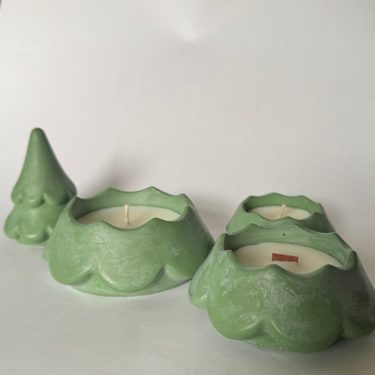 Three small green sculptural christmas tree  candle holders on a white sheet of paper, with a black patterned fabric visible at the bottom edge.