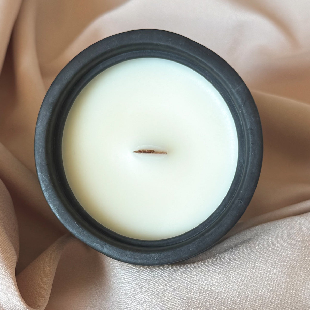 White candle in a black concrete candle jar on beige fabric